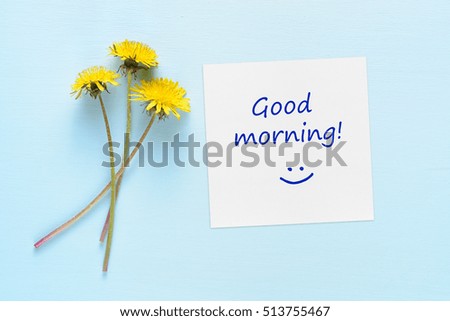 Dandelion flowers and paper with Good morning text on blue table
