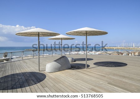 wooden deck with modern stone benches and sun umbrella patio. View to the sea shore