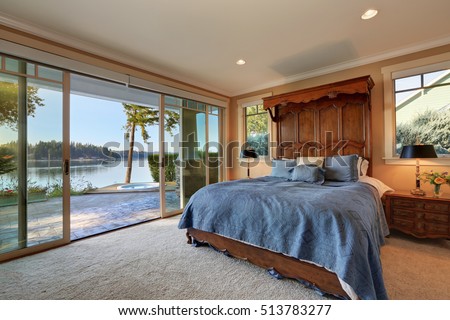 Master bedroom interior with glass wall. Opened sliding doors lead out to the back yard with jacuzzi . Bed with high wooden carved headboard . Carpet floor. Northwest, USA
