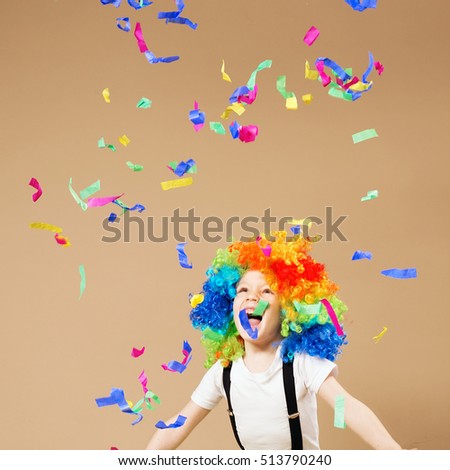 Little boy in clown wig jumping and having fun celebrating birthday. Portrait of a child throws up a multi-colored tinsel and confetti. Birthday boy. Brazilian Carnival. Venice Carnival. Royalty-Free Stock Photo #513790240