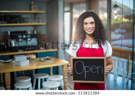 Portrait of smiling waitress showing slate with open sign in cafe