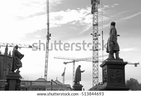 Black-and-white image. Statue on background of construction cranes. Berlin, Germany