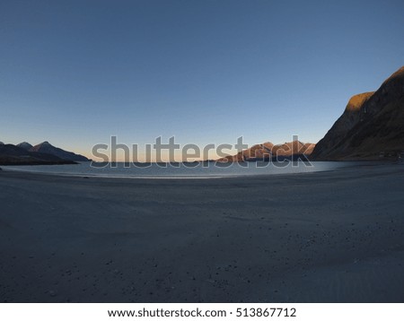 beautiful calm blue waves hitting white frozen sandy beach in late autumn in the arctic circle with deep mountain and open sea view on clear sky background