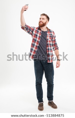 Full length portrait of a cheerful bearded man in plaid shirt taking selfie over white background