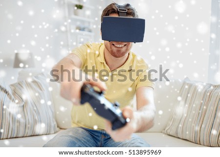 technology, augmented reality, gaming, entertainment and people concept - happy young man with virtual headset or 3d glasses with controller gamepad playing racing video game at home over snow