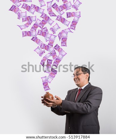 Indian/Asian handsome businessman catching flying newly launched 2000 rupees currency notes in his clay piggy bank/ money box, isolated over white background