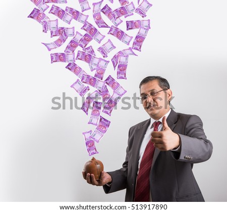 Indian/Asian handsome businessman catching flying newly launched 2000 rupees currency notes in his clay piggy bank/ money box, isolated over white background
