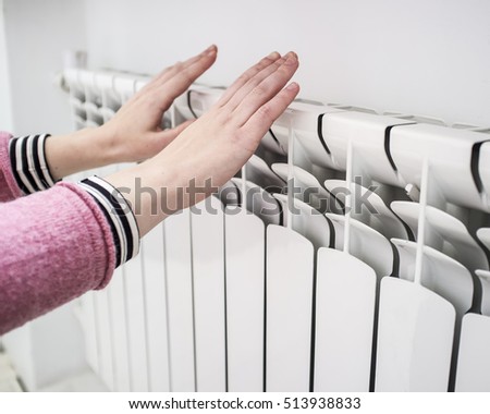 Girl warms the frozen hands above a hot of the radiator, close up
