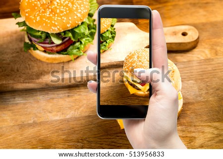 Woman takes a picture smartphone eating fast food. Delicious homemade burgers.