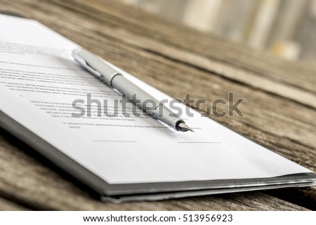 Ink pen lying on a contract or application form, low angle view. Royalty-Free Stock Photo #513956923