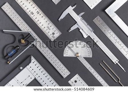 Neatly arranged metal right angle squares, calipers, protractors, rulers and other  measuring hand tools on dark gray background