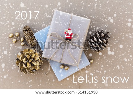 Christmas greeting card with snow and the words let is snow and 2017.present wrapped craft paper tied with natural thread on a craft background with Golden thread,fir cone,skein of thread, santa claus