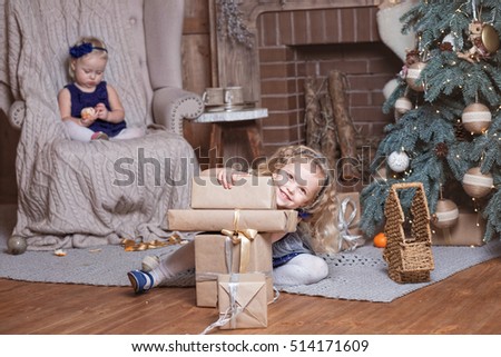 Adorable little girls eating tangerines and playing with a Christmas gifts by a Christmas tree in living room 
