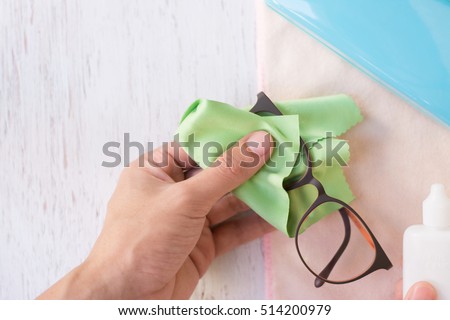 Close up cleaning glasses by microfiber cloth for cleaning lens and glasses concept.Close up cleaning glasses by microfiber cloth on white wood table.cleaning concept.