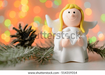 Toy angel with book in hand on the background of blurred lights garland with pine cone