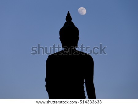A moon shines in a sky over a large silhouetted Buddha statue in Bangkok, Thailand. 