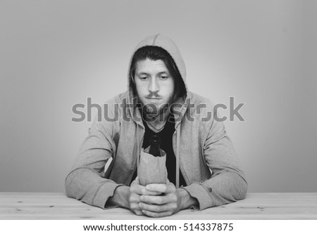 monochrome picture of youth beer alcoholism concept, addicted young bearded man wearing hoodie sitting with empty lager bottles in different colors 