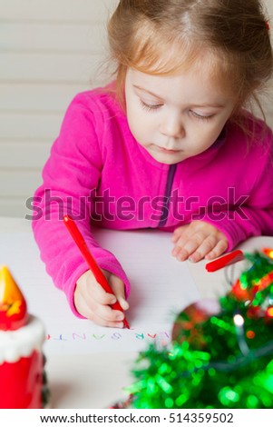 Little girl writes a letter to Santa. A child draws a Christmas picture.