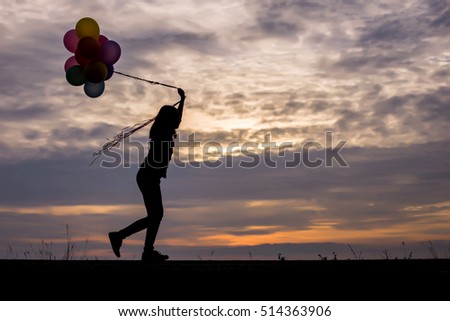  silhouette of Young woman holding colorful of balloons with sunset