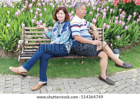 couple elderly man and woman sitting on bench in flower garden