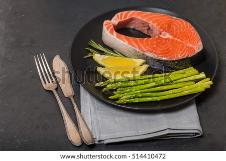 Delicious portion of fresh salmon steak with aromatic herbs, spices and vegetables on black background - healthy food, diet or cooking concept