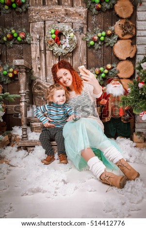 Happy red hair mother and two years old son boy are sitting in christmas decorations and taking selfie