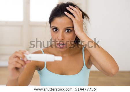 young attractive latin woman holding pregnancy test on bed at home looking at positive result in shock and stress having surprise in girl unwanted maternity concept 