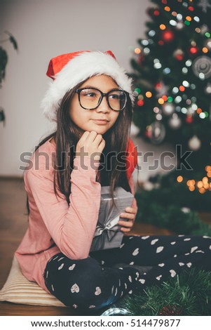 Girl wearing santa hat holding gift and contemplating