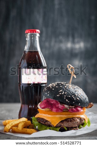 Gourmet black burger with berry sauce, french fries and beer on wooden table and dark background