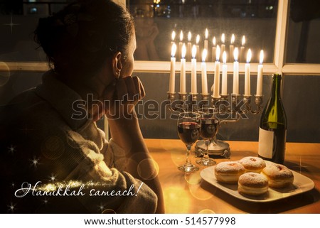 Greeting Card Hanukkah Sameach. Low key Image of jewish holiday Hanukkah (holiday of lights) with menorah, burning candles, donuts and wine. View to the night Tel Aviv from window. Jewish Girl