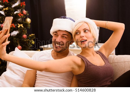 Picture of happy Christmas couple making self photos on mobile or smart home while celebrating New Year or Christmas at home