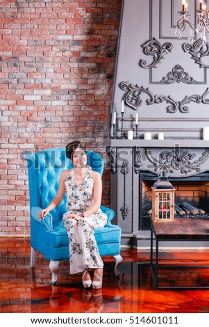 Beautiful woman with blue eyes and curly hair in dress on luxory interer background the fireplace chandelier.  sofa