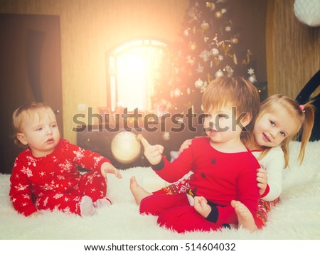 Three cute children playing on the bed in their pajamas on the background of the Christmas tree. Christmas night