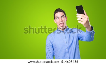 Naughty young man taking a selfie with his smartphone against green