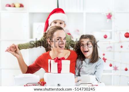 Two kids and their mother are opening Christmas presents in their living room. They are having a lot of fun.
