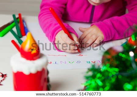 Little girl writes a letter to Santa. A child draws a Christmas drawing.