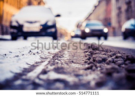 Winter in a big city, on a snowy street light riding car headlights. Close up view from the road level, image in the blue toning