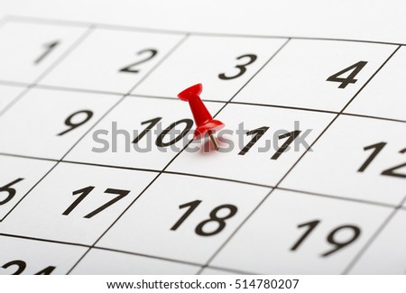 Pin on the date number 11. The eleventh day of the month is marked with a red thumbtack. Focus point on the red pin.