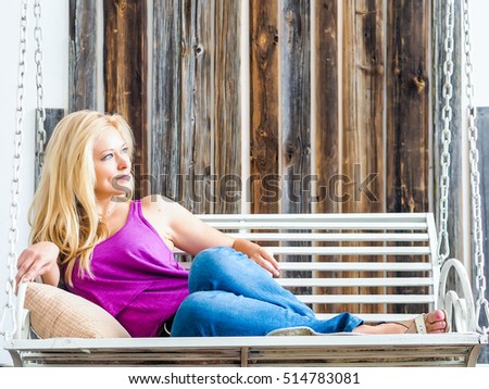 Russian beautiful blonde in blue jeans and a purple shirt on a swing