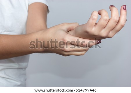 Close up woman's hand holding her wrist  over gray background