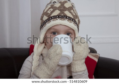 Light hair girl in warm hat and mittens drink hot chocolate.