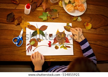Sweet child, boy, applying leaves using glue while doing arts and crafts in school, autumn time
