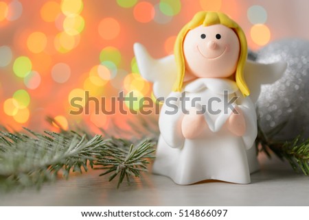 Toy angel with a book and a fir branch on a background of blurred lights garland