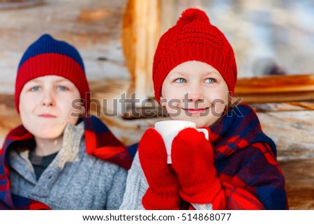 Kids outdoors on beautiful winter day drinking hot chocolate in front of log cabin vacation house