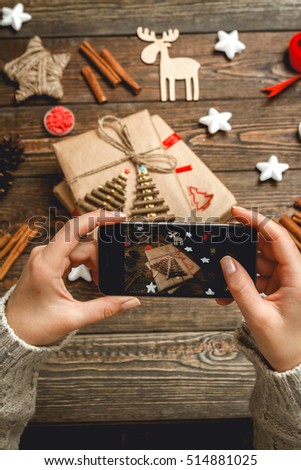 Girl in a cozy knitted sweater makes the photo on the phone Christmas accessories and handmade gifts on dark wooden desk