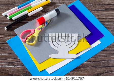 The child carves the details greeting cards image of the Jewish holiday of Hanukkah. Glue, scissors, paper, leaves on wooden table. Children's Art Project, needlework, crafts for children.