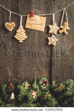 painted by gingerbread cookie greeting card with the words on the rope above the spruce branches on a dark background.