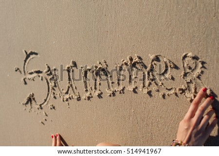 girl's hand makes the inscription on the sand "Summer"