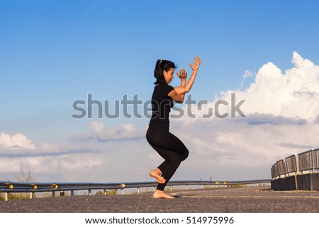 Young woman exercises yoga in the road on the mountains, blue sky, white clouds.