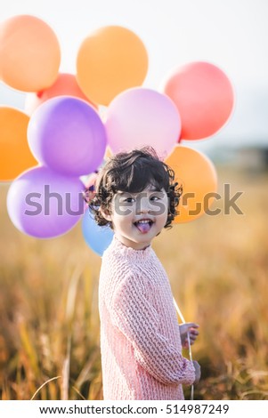 Little girl playing with balloons on wheat field
